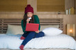 © TheVisualsYouNeed - young beautiful happy Asian Korean woman in winter hat relaxed on bed holding credit card using laptop computer for internet banking and online shopping
