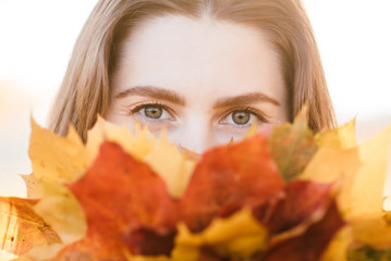 Beautiful young happy girl with a bright red-yellow autumn leaf in the park