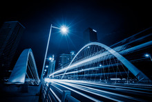 Car Light Trails On Steel Bridge With City Skyline.