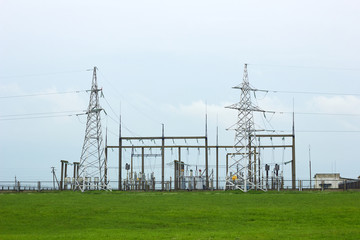 Transformer substation high voltage electrical network in the meadow on beautiful flat land scenic background. Industrial energy. Metal structures, insulators and cable, copy space