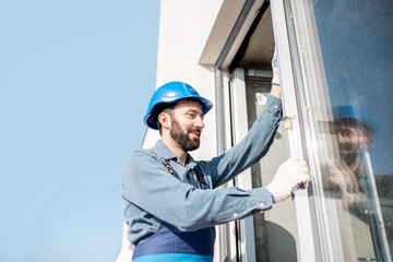 Workman in uniform mounting windows checking the level on the white building facade