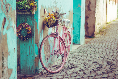 Obraz rower  rozowy-rower-vintage-z-koszem-pelnym-kwiatow-obok-starego-budynku-w-kolorze-turkusowym-w-hiszpanii