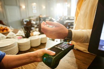 Cashier holding payment machine while one of clients with smartwatch keeping his wrist over it