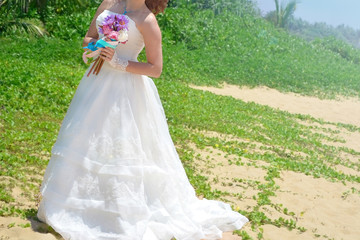 A young bride in a white airy dress is standing with a bouquet of lotuses. girl on a tropical beach on the island of Sri Lanka