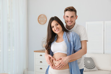 Sticker - Pregnant woman and her husband showing heart with hands at home