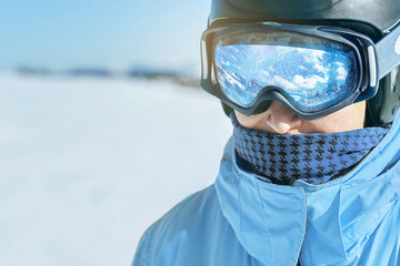 Wall Mural - Close up of the ski goggles of a man with the reflection of snowed mountains.  A mountain range reflected in the ski mask.  Man  on the background blue sky. Wearing ski glasses. Winter Sports.