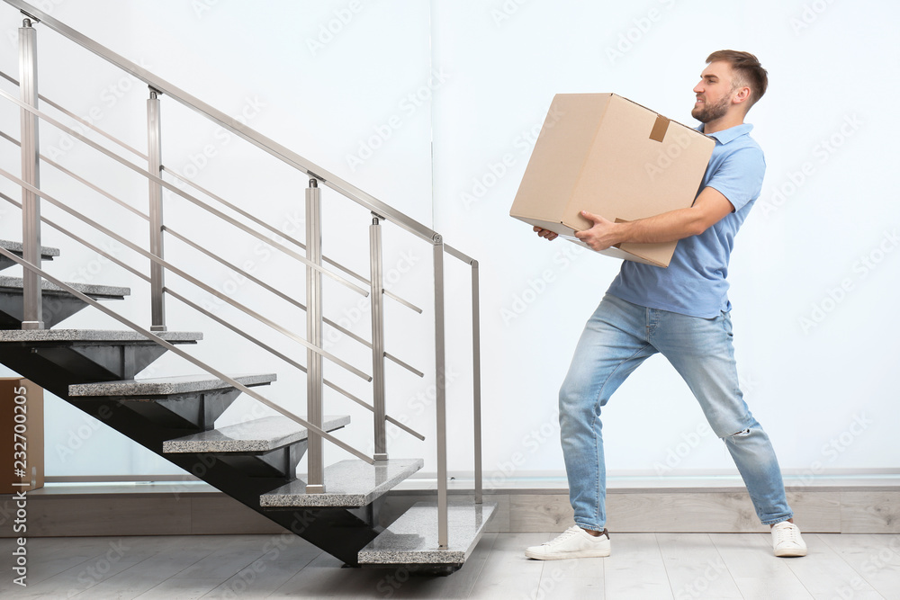 Young man carrying carton box indoors. Posture concept - obrazy, fototapety, plakaty 