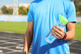 Fototapeta Most - Sporty man holding bottle of water at stadium on sunny day, closeup