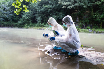 two scientists in protective suits taking water samples from the river.