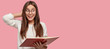 © wayhome.studio  - Photo of joyful attractive girl looks happily aside, wears white sweater, round eyewear, reads information from textbook, stands against pink background with free space for your advertisement