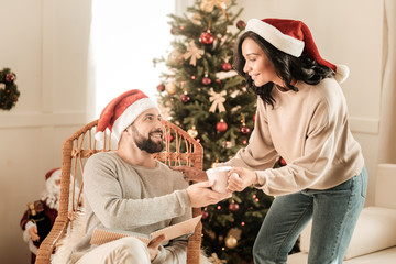 Care and support. Pleasant nice young woman looking at her boyfriend and giving his tea while expressing her care