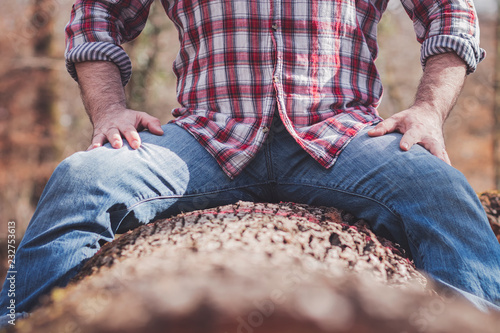 Strong Man In Plaid Shirt And Blue Jeans Sitting On A Cut Tree Trunk Legs Spread Stock Photo Adobe Stock