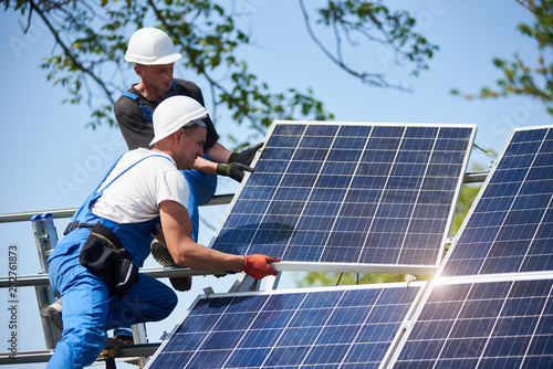 Two Workers Mounting Heavy Solar Photo Voltaic Panel On Tall