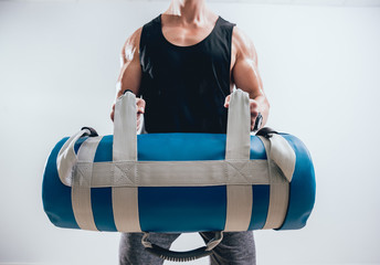 Athletic young man training with sandbags at gray background. Crossfit center