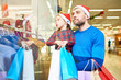 © Seventyfour - Adult bearded man and girl in Santa hats carrying paper bags and exploring shop window in mall