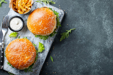 Tasty grilled home made burger with beef, tomato, cheese, cucumber and lettuce on a dark stone background with copy space. Top view. fast food and junk food concept