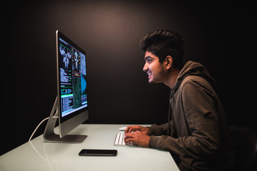 Handsome indian male programmer, IT person, hacker, works in computer on internet, black background.