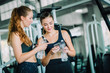 © Shutter B - Fit beautiful young woman athletes in fitness clothes relaxing after workout in gym. Couple women standing holding water in bottle and using fitness app smartphone. Healthy, Sport, Lifestyle concept.