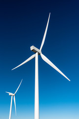 Close-up of two white wind turbines against a deep blue sky background