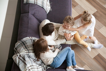 married couple with little preschool children sitting on couch in living room at new modern wealthy 