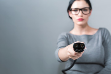 Young woman with an electric vehicle charger on a gray background