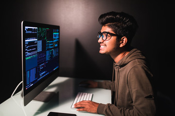 Program development concept. Young indian man working with computer on dark background