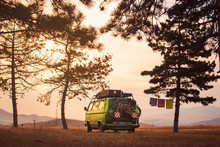 Old Timer Camper Van Parked On The Top Of The Hill Between Pine Trees In The Beautiful Sunset Sky