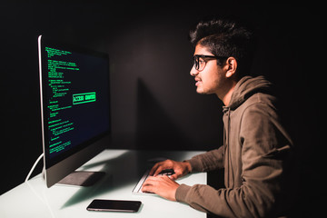 Indian man programmer working on desktop computer at white desk in office.