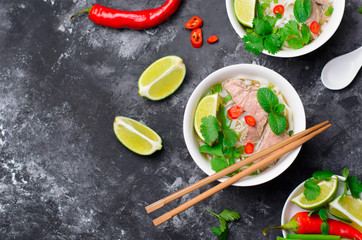 Wall Mural - Traditional Vietnamese Soup Pho Bo with Rice Noodles, Beef and Herbs on Dark Background