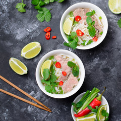 Wall Mural - Traditional Vietnamese Soup Pho Bo with Rice Noodles, Beef and Herbs on Dark Background