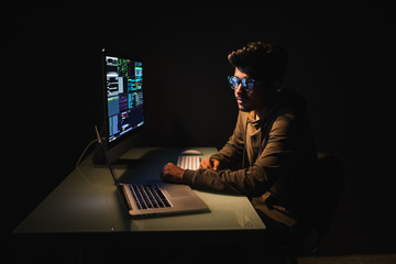 Indian male programer in dark room writing code or using computer and laptop for virus program for cyber attack