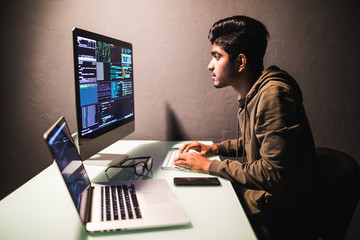 Indian Male programmer working on desktop computer at white desk in office.