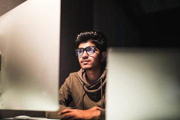 Young indian Man Sitting At Desk Working On Computer And Laptop At Home