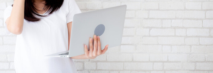 Wall Mural - Banner website asian woman standing holding laptop on brick cement wall background, girl working computer, business and lifestyle concept.