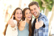 © Antonioguillem - Three happy friends smiling with thumbs up in the street