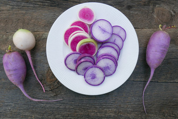 a plate of sliced white and purple radishes with whole vegetables on wood 