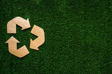 Wall Mural - Eco recycle sign made of craft paper on green grass background top view copy space