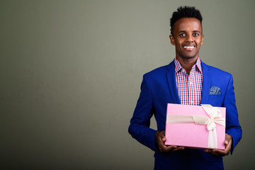 Wall Mural - Young handsome African businessman holding gift box against colo