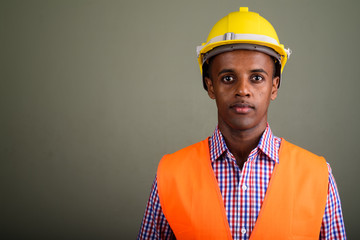 Young handsome African man construction worker against colored b