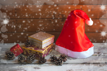 Santa hat, christmas gifts and  pine cones on aged wooden table near wooden wall