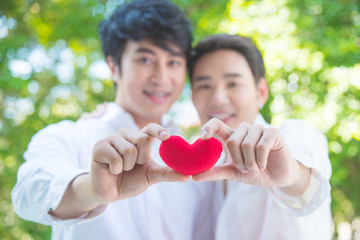 Young asian homosexual couple holding red color heart shape and smile together