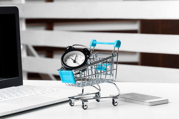 Wall Mural - Big alarm clock in shopping cart on a table