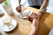 © NDABCREATIVITY - Close up of hands of couple sitting at the table and holding them together while drinking coffee