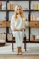 Wall Mural - beautiful woman sitting with cup of coffee and reading book in living room