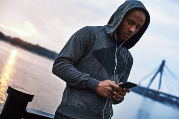 The young black athlete in hood is listening to music after training in the city