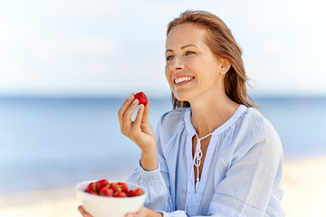 people and leisure concept - happy smiling woman eating strawberries on summer beach