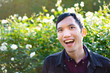 Portrait of young southeast asian man smiling and laughing happily on white roses background under the light of sunset in autumn