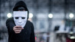 © zephyr_p - Mystery hoodie man with black mask holding white mask in his hand. Anonymous social masking or bipolar disorder concept.