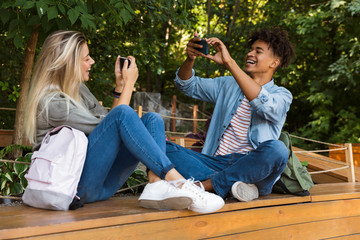 Wall Mural - Young loving couple take selfie by mobile phone outdoors in park.