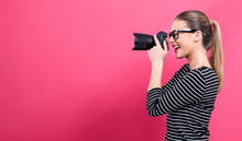 Young Woman With A Professional Digital SLR Camera On A Pink Background